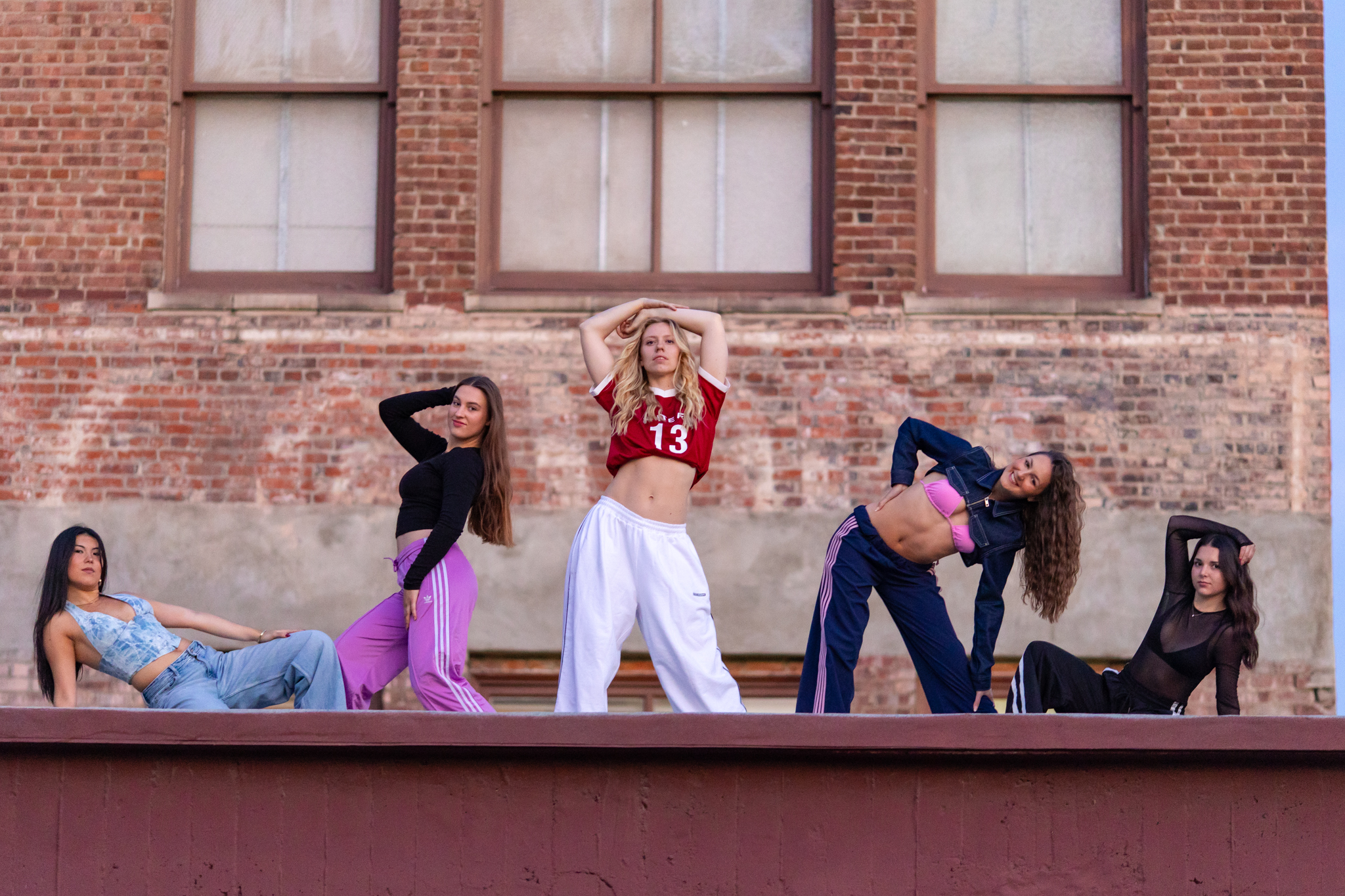 Five international dancers pose on an urban rooftop in front of a historic brick building during a Los Angeles dance photoshoot, showcasing different styles, personalities, and performance poses.